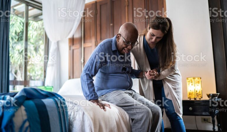 Home caregiver helping a senior man standing up at home