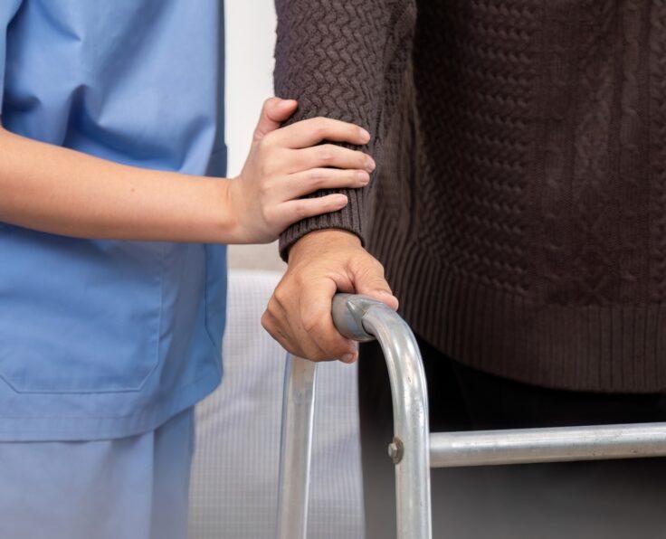 Caregiver Assisting Elderly Patient with Physical Therapy Using Walker in Home Setting for